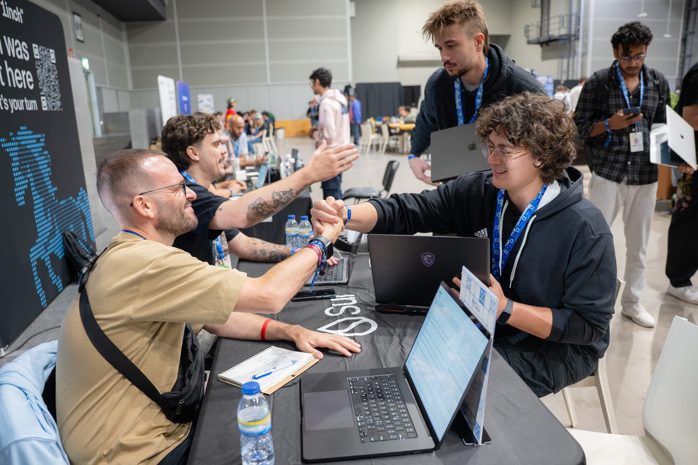 Mentors and builders around a table of laptops at ETHGlobal Lisbon, one pair fist-bumping.