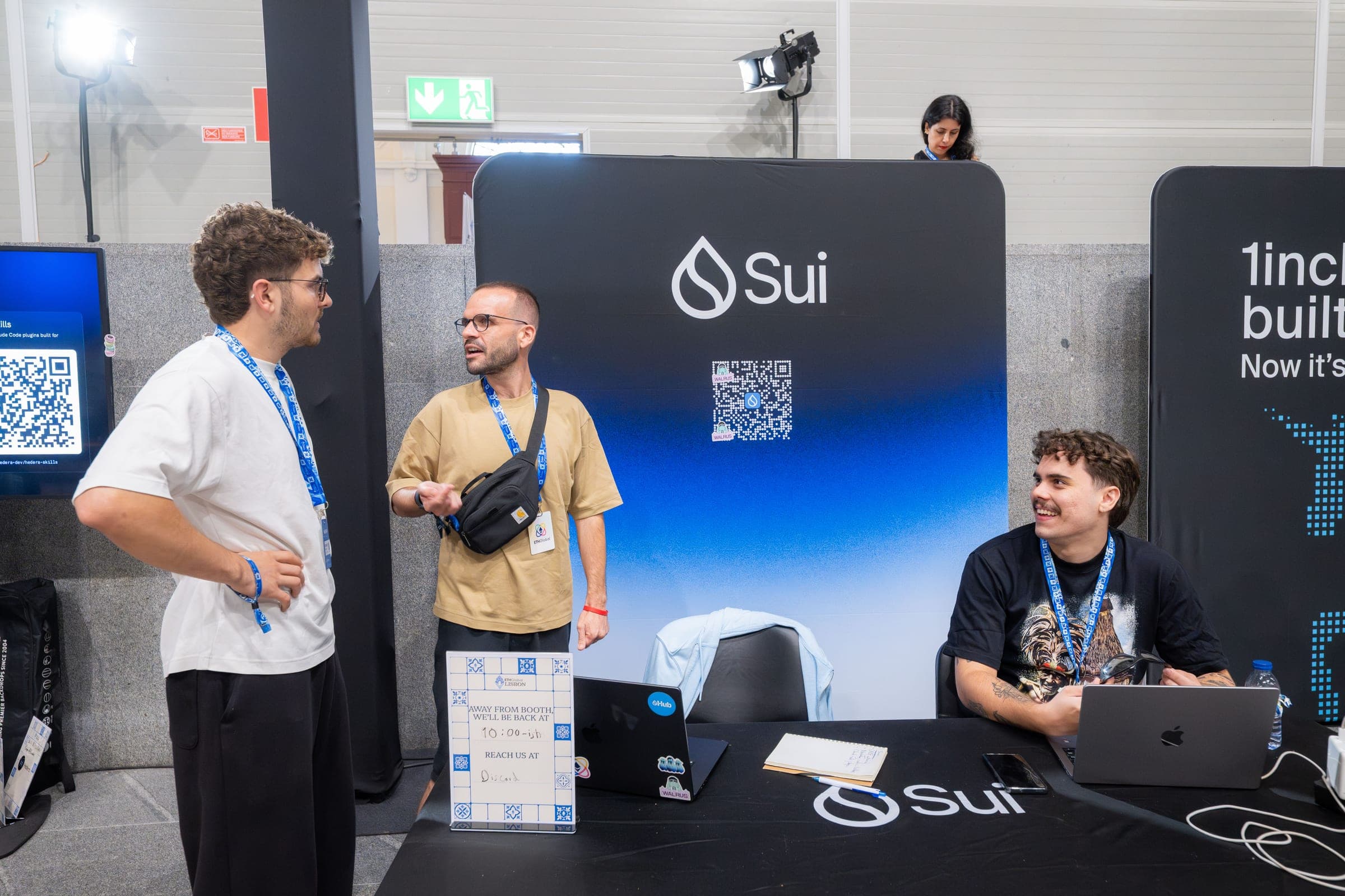 Two mentors talk with a builder in front of the Sui booth at ETHGlobal Lisbon.