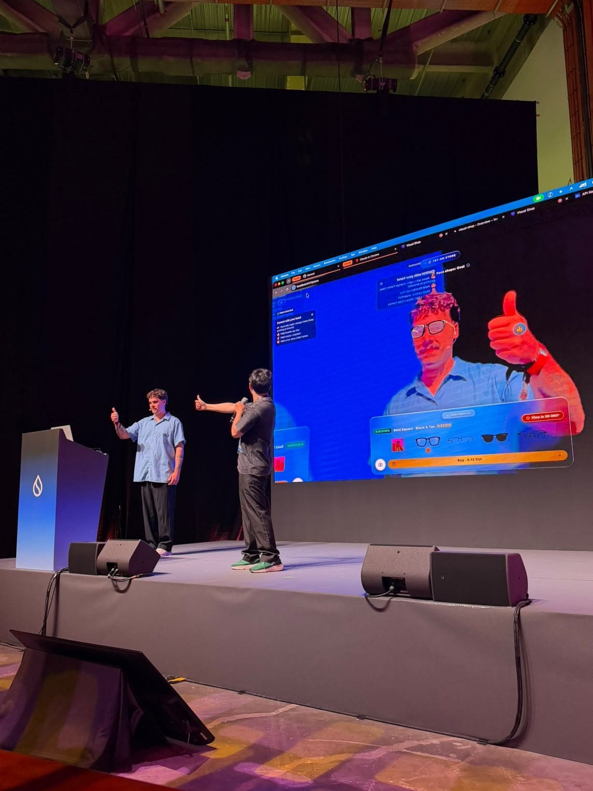 Two people on stage give a thumbs-up during a live demo of a virtual glasses try-on at Sui Basecamp.