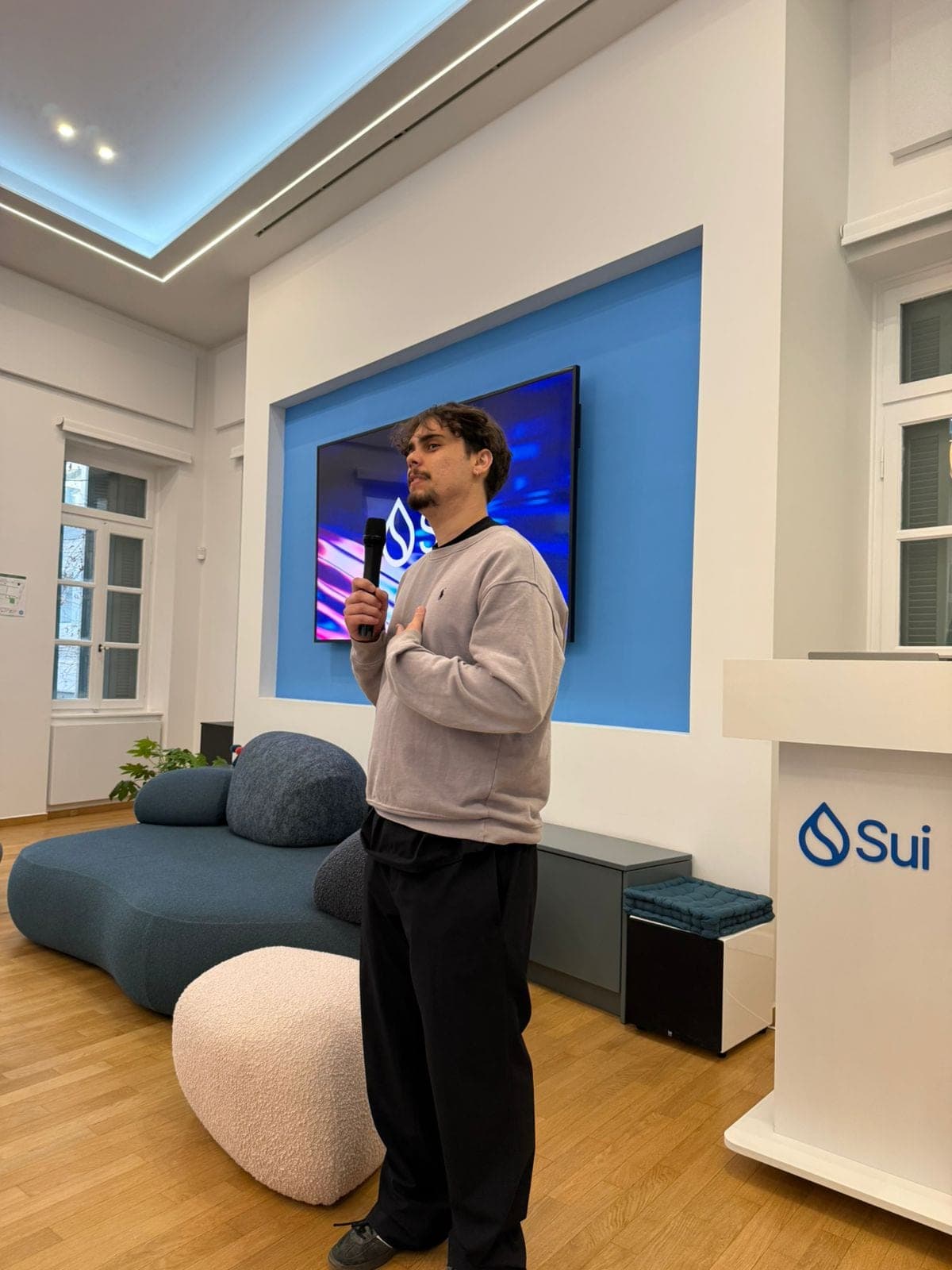 Guilherme speaks into a microphone in front of a Sui screen at SuiHub Athens.